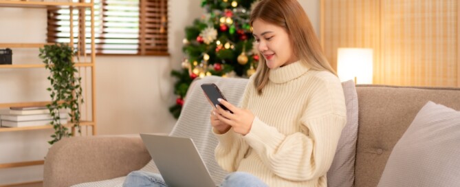 girl sitting on couch looking at her phone near Christmas tree